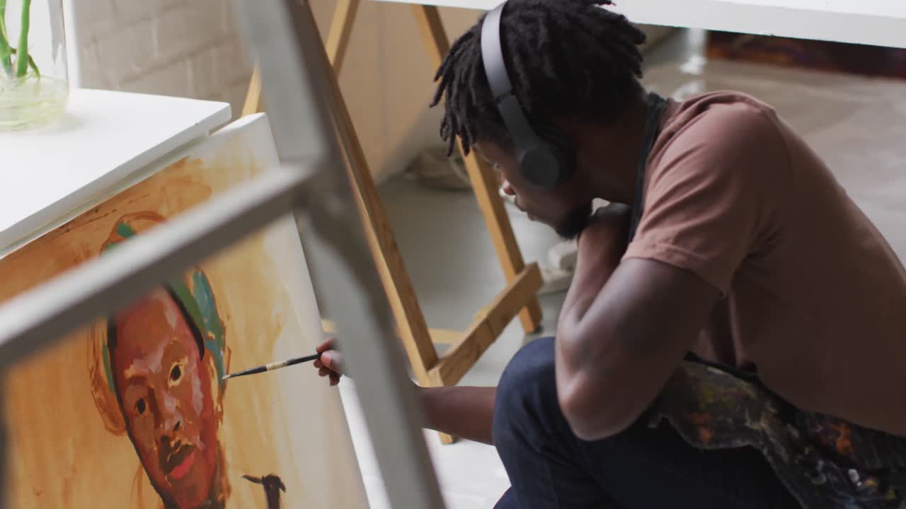 artista afroamericano de sexo masculino con auriculares pintando en lienzo en un estudio de arte