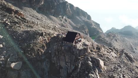 wooden cabin built on the steep facade of a rocky mountain in the swiss alps, sunrise captured by drone