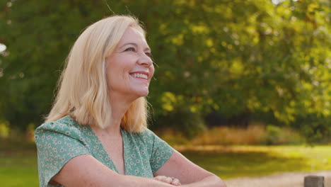 Portrait-Of-Laughing-Mature-Or-Senior-Woman-Leaning-On-Fence-On-Walk-In-Countryside