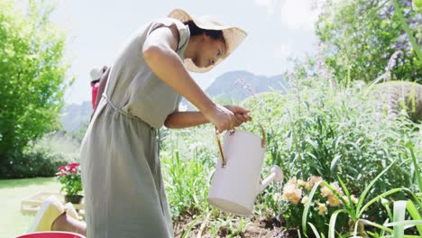 happy african american mother watering flowers in sunny garden, family in background, slow motion