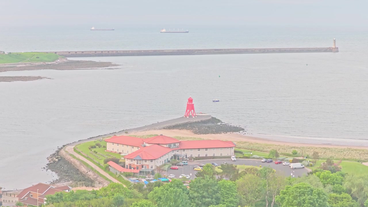 Il faro di South Shields si erge all'ingresso del porto del fiume Tyne, dove l'estuario incontra il Mare del Nord, con frangiflutti, edifici costieri e navi da carico al largo, ascesa del drone.