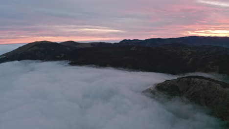 Misty-mountains-at-dawn-with-soft-light-breaking-through-the-clouds,-aerial-view