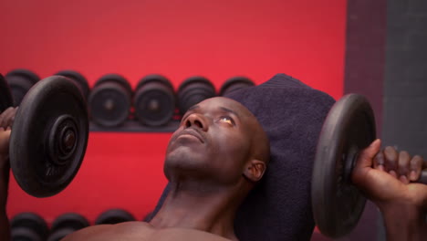 fit man lying on exercise table holding dumbbell