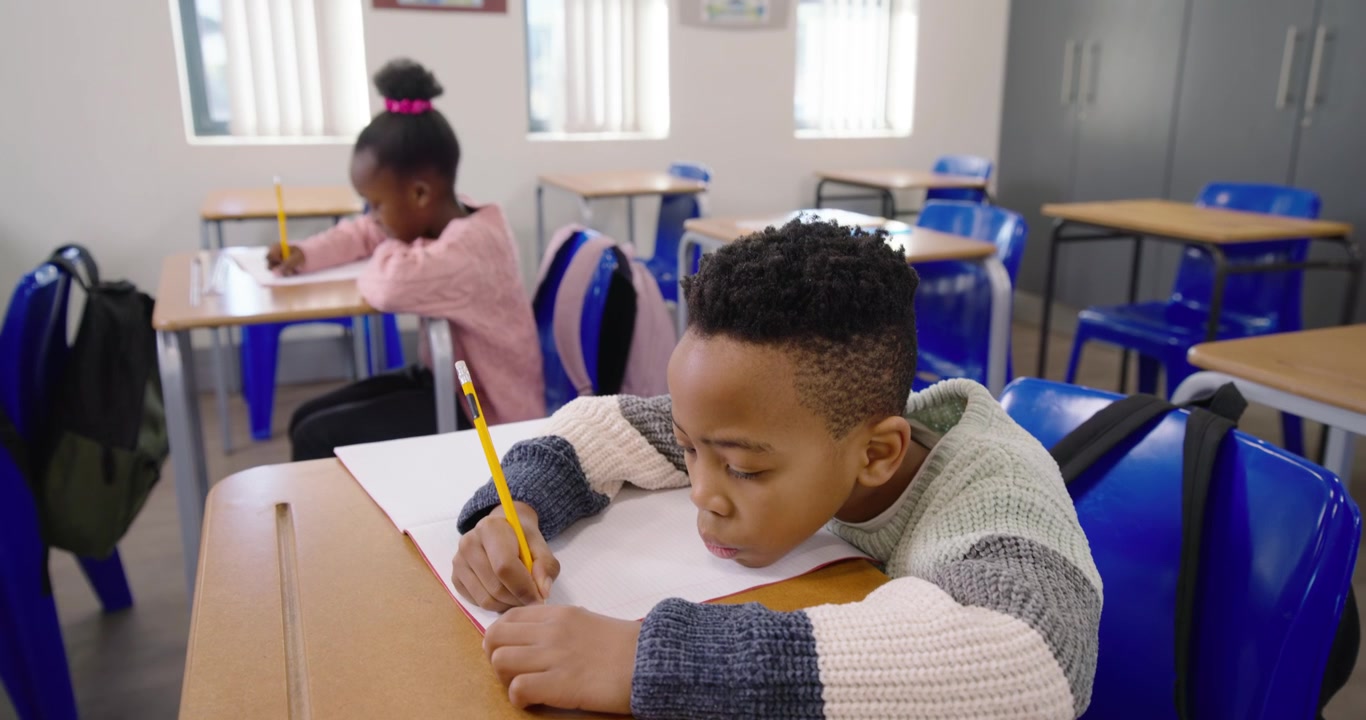 Classmates starting lesson and writing on looseleaf at desks with yellow pencils near windows