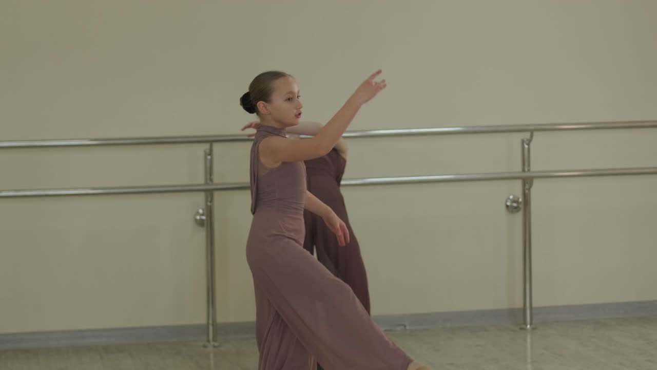 검은색 댄스웨어를 입은 젊은 발레 학생들이 나무 바닥과 벽에 장착된 바를 가진 넓은 발레 스튜디오에서 자세를 연습하는 그룹.