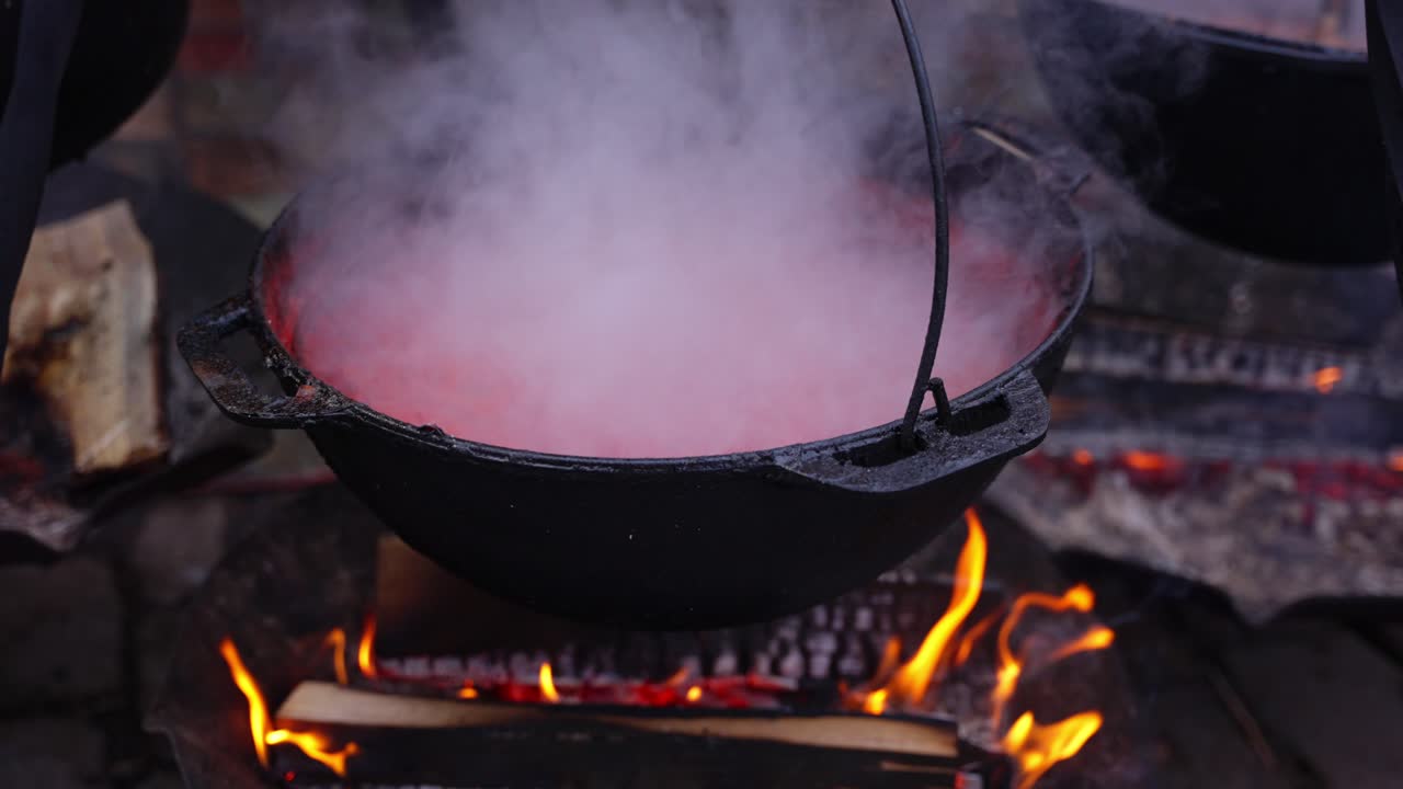 Zuppa di cibo da strada calda che bolle su fiamma libera in una postazione di cucina all'aperto, vapore che sale al rallentatore