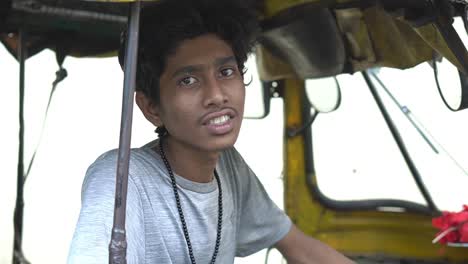 Zeitlupenaufnahme-Eines-Jungen-Indischen-Autofahrers-In-Grauem-T-Shirt,-Der-Im-Auto-Sitzt-Und-In-Die-Kamera-Schaut