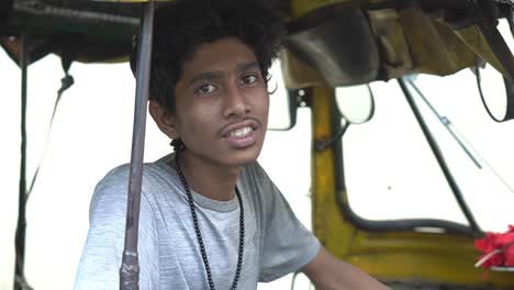 slow motion shot of an young indian auto driver in grey t-shirt sitting inside the auto and looking at the camera