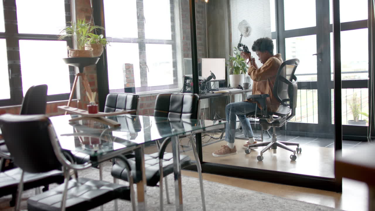 Happy african american man sitting at desk making live podcast from home, copy space, slow motion