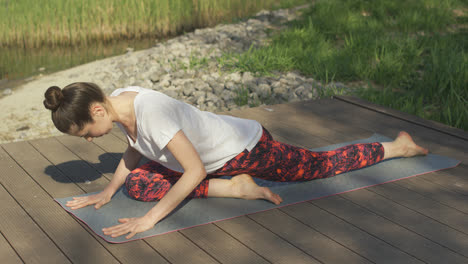 Young-woman-doing-yoga-exercises-on-mat-in-summer-day