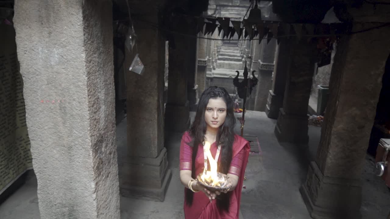 hermosa niña india en un antiguo pozo de paso con sari rojo indio tradicional, joyas de oro y brazaletes con placa de fuego