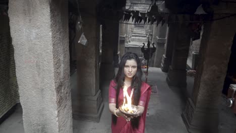 beautiful-Indian-girl-in-old-stepwell-wearing-traditional-Indian-red-saree,-gold-jewellery-and-bangles-holding-fire-plate