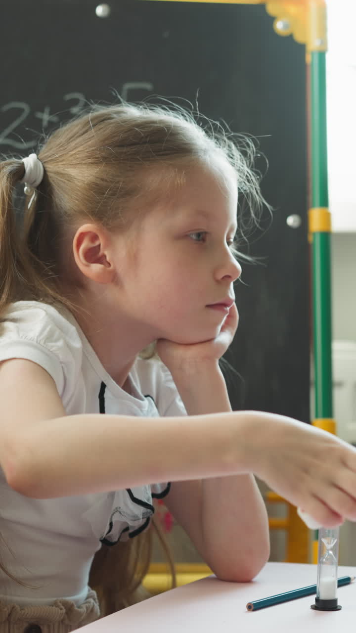 Caring long haired girl fans little brother with number cards in classroom on hot day. Sister helps toddler kid to cool down at homework in nursery