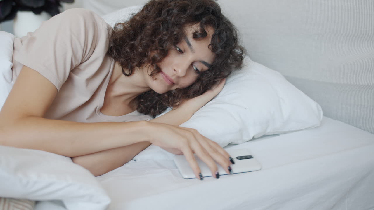 Kvinde vågner op i seng med telefon