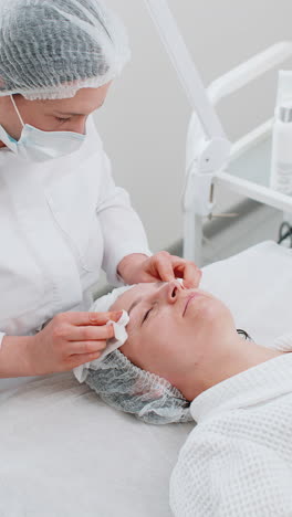 cosmetologist doctor wipes woman face and neck cleaning procedure with cotton pads in beauty clinic