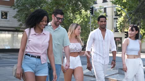 cheerful diverse friends talking as they walk on city street