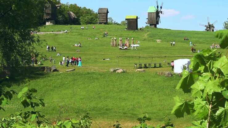 Menschen ruhen auf grüner Wiese im Frühlingspark. Grüne Bäume und alte Windmühle