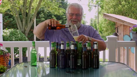 a man with a beard sits at an outdoor table on a sunny day, surrounded by different beer bottles. he is opening bottles and preparing to enjoy a relaxing moment outside