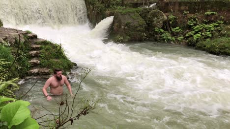 man swimming in a cold mountain river under a waterfall
