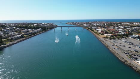 Aerial-tracking-shot-of-boats-in-channel-of-water-and-cars-driving-over-bridge-in-background