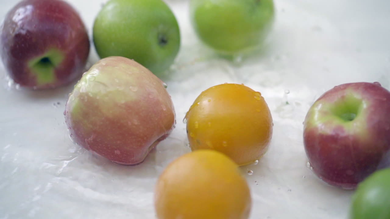 Slowmotion af æbler og appelsiner i vand på hvid baggrund.