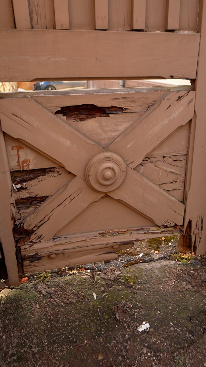 Close-up of a weathered wooden gate with peeling paint and visible decay, capturing aged craftsmanship, outdoor wear, and neglected rustic architectural detail.