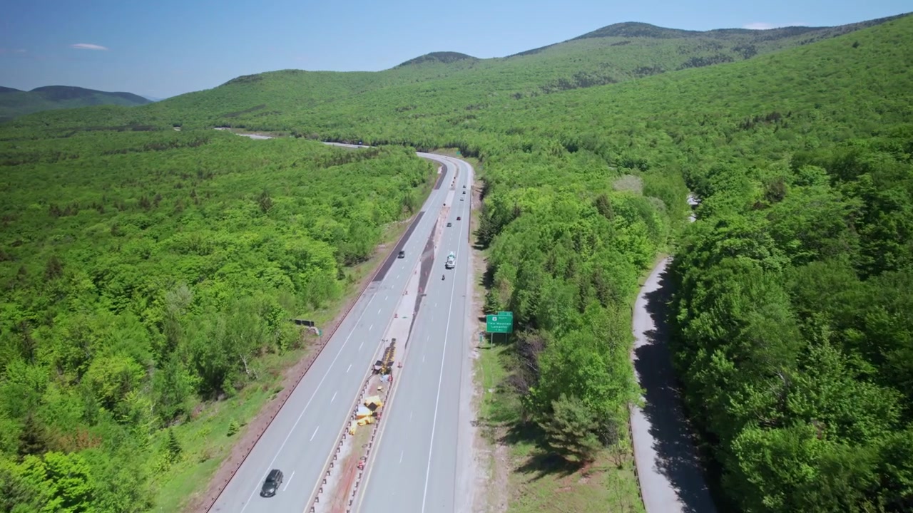 Biler kører gennem motorvejspas gennem tæt, skovklædt terræn i White Mountain National Forest i New Hampshire, USA. - luftfoto