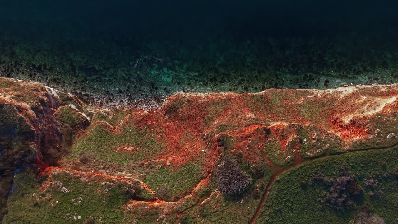 Sunlight shines on rocky coastline with green grass and clear water at midday showing the natural landscape in detail