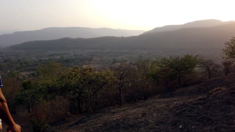 joven parado y viendo la puesta de sol a través de las montañas y un valle con hermosos paisajes