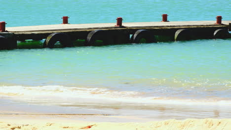 Concrete-jetty-jutting-into-clear-blue-water-of-Struisbaai-harbour,-telephoto