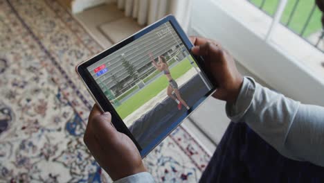 Compuesto-De-Un-Hombre-Sentado-En-Casa-Viendo-Un-Evento-De-Salto-De-Altura-De-Atletismo-En-Una-Tableta