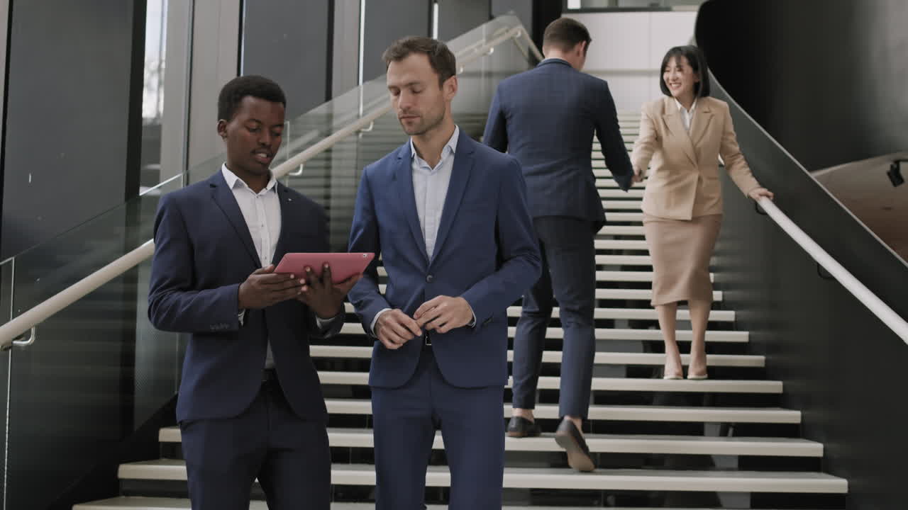 dos gerentes masculinos bajando las escaleras mientras usan la tableta