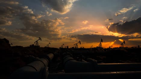 pipeline and working oil pump jacks in a against sunset extracting crude oil. pumping fossil oil is one of the methods of energy generation from renewable energy sources