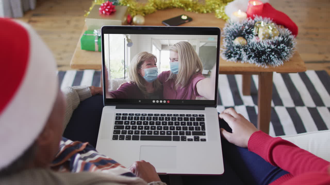 아프리카계 미국인 어머니와 딸이 스크린에서 가족과 함께 크리스마스 비디오 통화를 위해 노트북을 사용합니다.