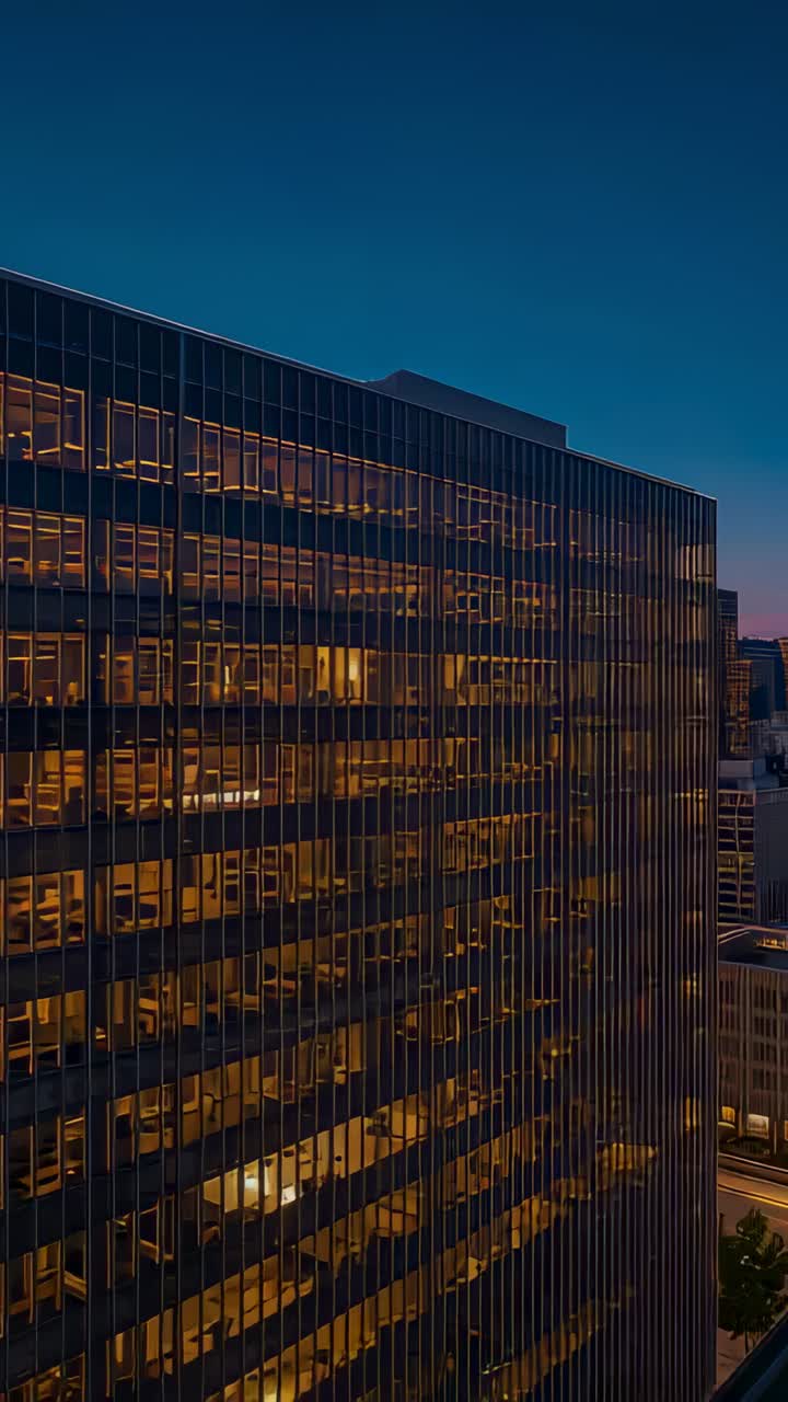 Vertical video: Dusk settling, panning camera revealing glass-clad high-rise facade and lit windows
