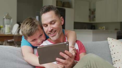 Glücklicher-Kaukasischer-Vater-Mit-Sohn,-Der-Im-Wohnzimmer-Sitzt-Und-Ein-Tablet-Benutzt