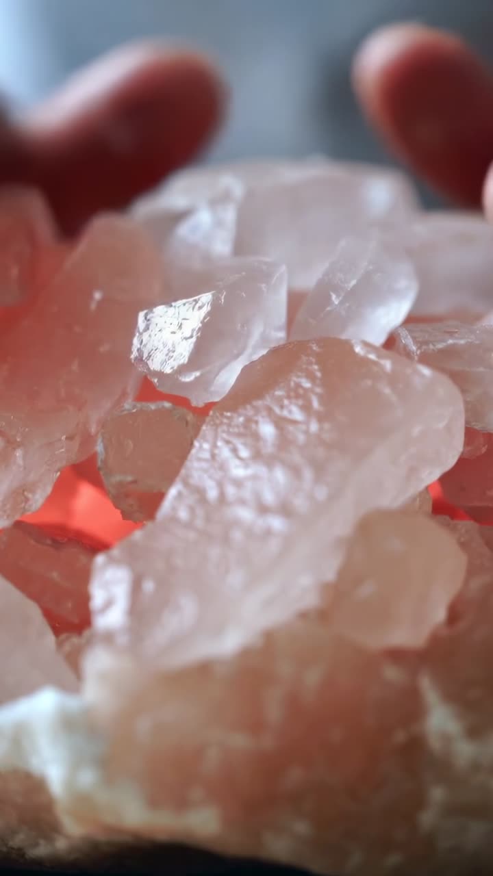 Mãos adultas se aproximando, colocando, ajustando e pressionando cristais rosa sobre a mesa, revelando uma base iluminada.
