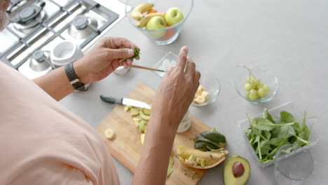 High-angle-of-senior-biracial-man-preparing-fruit-and-vegetable-smoothie-in-kitchen,-slow-motion