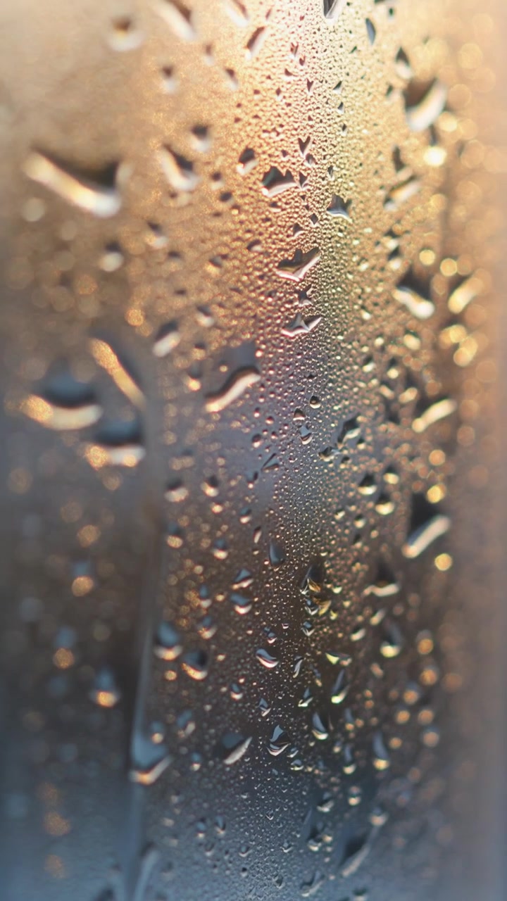 Foto macro de gotas de condensação de água em vidro retroiluminadas pela luz quente do pôr do sol dourado