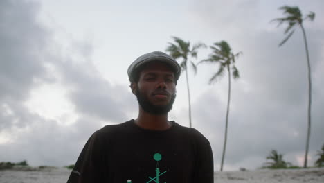 medium shot of a young black man on an exotic beach with palm trees in the background