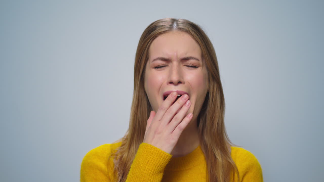 Portrait of smiling woman yawning at camera on grey background in studio.