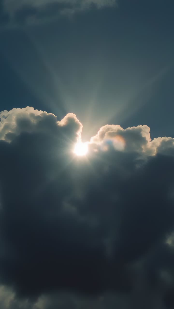 Vertical video: Peeking sun breaking through cumulus cloud from ground, casting rays and lens flare