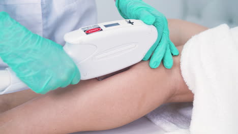 cosmetologist in gloves does laser epilation of client legs