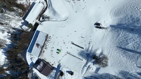 high altitude top down shot of bottom of ski run, static shot of skiers arriving at base of mountain lining up for the chairlifts