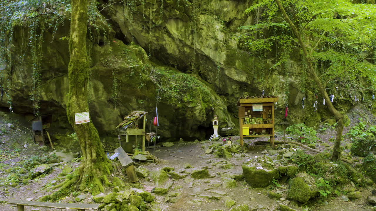 Panning from the right to the left side of the frame in front of a hanging rock where altars, sacred images and icons are displayed at Indipasha Sanctuary beside Strandzha Mountain, in Bulgaria.