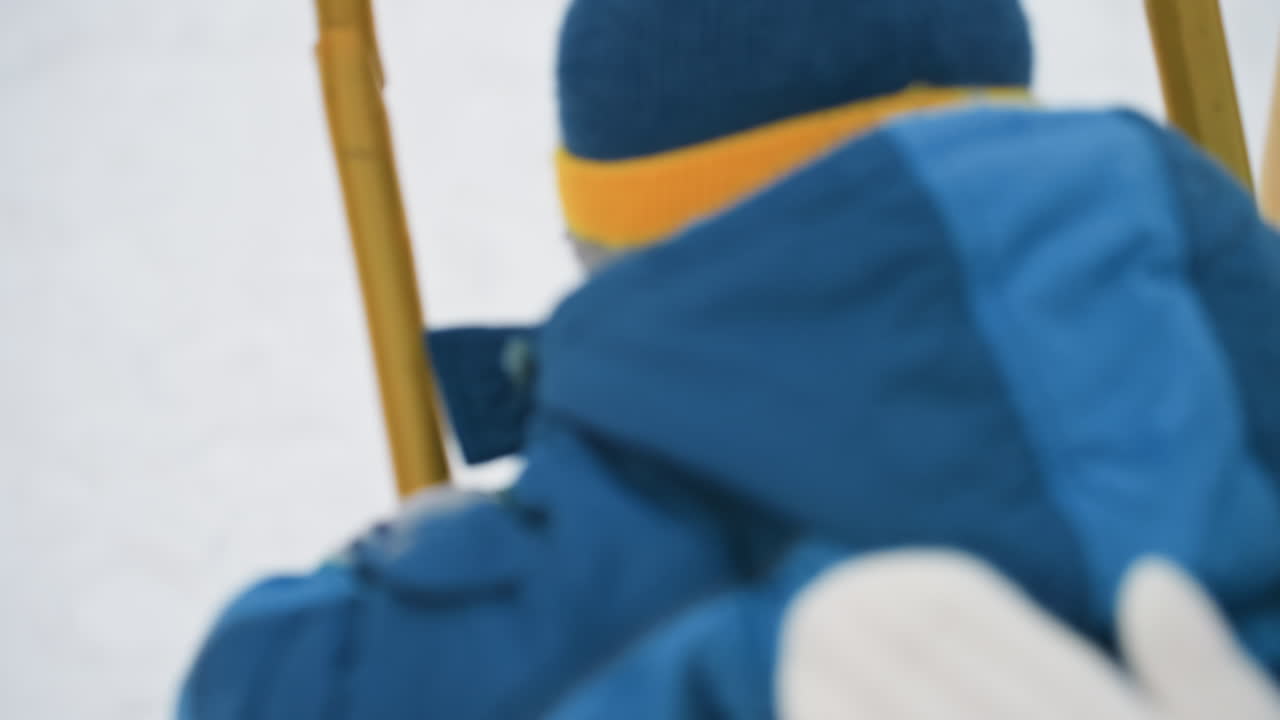 Son back on winter swing closeup, bundled child in blue coat and pompom hat, rope and grip details, offscreen mother hand gently steadying, quiet reflective mood, fabric texture and soft breath