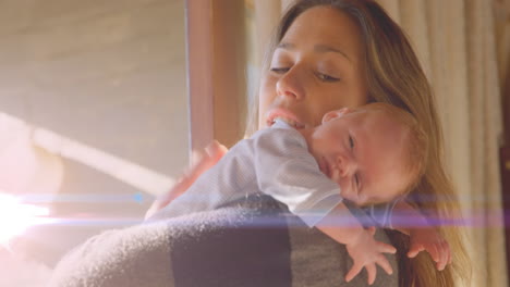 animation of glowing spots over happy caucasian mother with sleeping baby