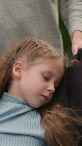 preschooler girl with cerebral palsy sleeps in wheelchair after therapy. mother pushes medical equipment with daughter walking on road in town closeup