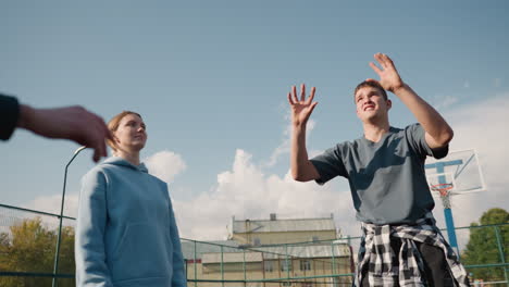 training session of beginners playing volleyball with coach wearing plaid shirt around waist in open court, background featuring building and fence, practicing volleyball techniques