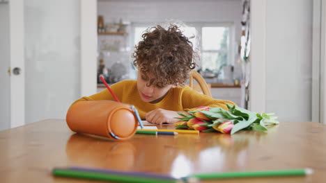 young boy at home with bunch of flowers writing in mothers day card